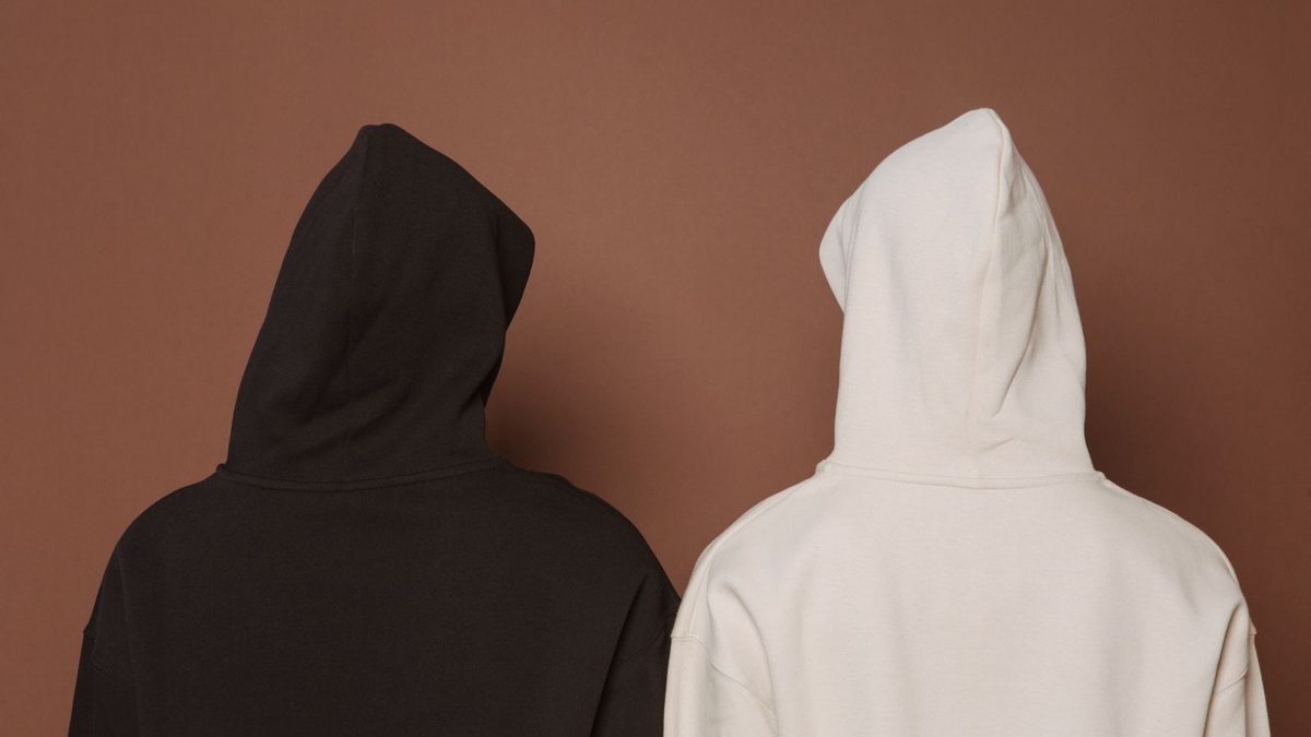 Two people seen from behind in plain hooded sweatshirts, one espresso and one oat, against a terracotta wall