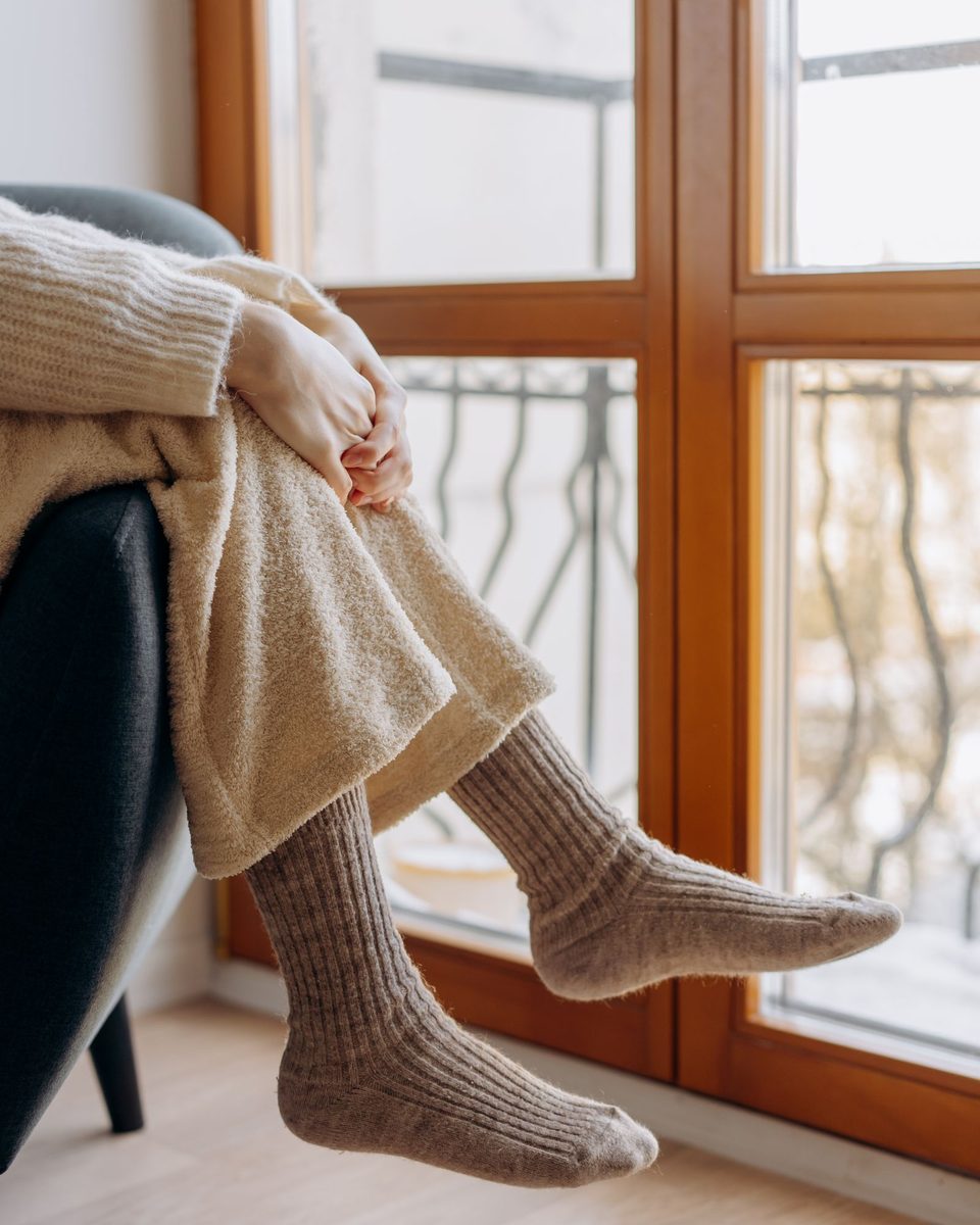 Feet in ribbed oatmeal wool socks resting on a window sill
